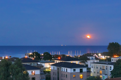 Aufgehender Vollmond über der Ostsee - im Hintergrund Mecklenburg-Vorpommern, im Vordergrund die Lichter von Dahme in der Abenddämmerung - Ostholstein